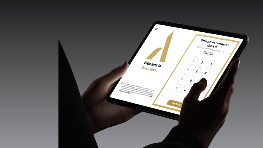 Guest holding a tablet displaying the Aura salon check-in screen and phone-number keypad