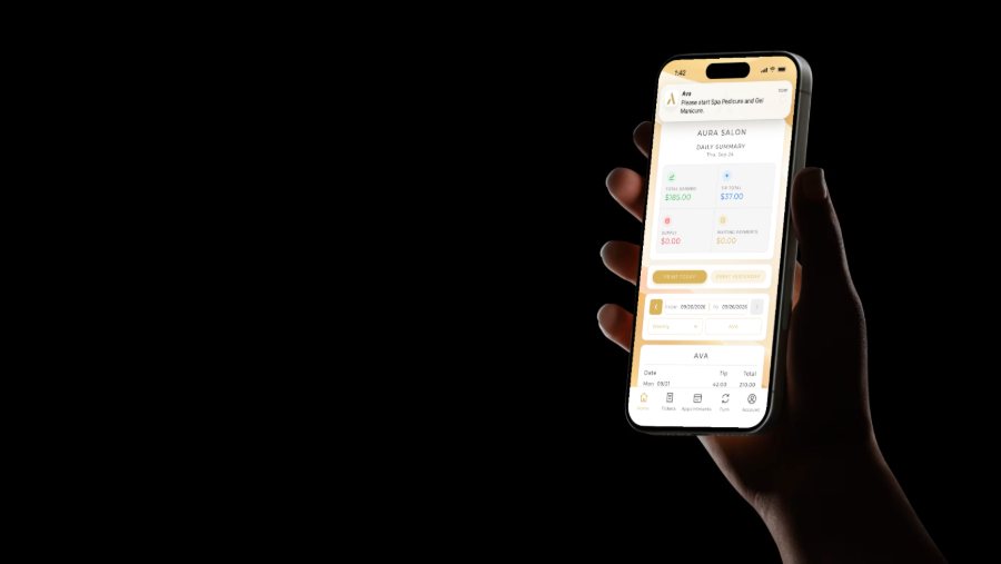 A hand holding an iPhone on the Aura Staff Home tab as a notification for Ava arrives: Please start Spa Pedicure and Gel Manicure.